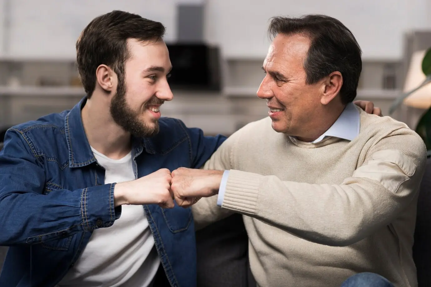 A father and son exchanging a fist bump in a living room.